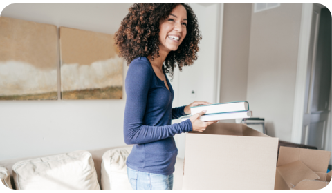 Woman packing up books in a moving box smiling with excitement 